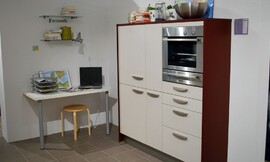 Voorbeeld van een werkplek in de hoek van de keuken. Een simpel tafelblad aan de muur met twee tafelpoten. Keukenkast met gebroken witte fronten en wangen van donker hout. Ingebouwde magnetron-oven-combinatie. Zuordnung: Stil Klassieke keukens, Planungsart Keuken met keukeneiland