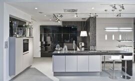 Greeploze keuken met stenen aanrechtblad en zitgelegenheid aan bar. Strakke lichtgrijze fronten en hoogglans zwarte fronten. Kraan centraal op keukeneiland. Zuordnung: Stil Moderne keukens, Planungsart U-vormige keuken