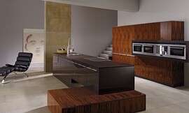 Deze keuken leunt optisch op de edele santos-palissander met diepe tekening. Deze wordt gecomplementeerd door de donkerbruine hoogglans fronten van het keukeneiland. Zuordnung: Stil Design-keukens, Planungsart Keuken met keukeneiland