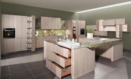 Moderne behaaglijkheid en absolute elegantie. Het oppervlakte is gebeitst in de tint &quot;zilver eik&quot;, waardoor deze topkeuken herinnert aan de natuurlijkheid van oude versleten houtplanken. Het binnenwerk van de lades in massief notenhout biedt een aangenaam, warm contrast met de koelere tint van de buitenkant van de meubels. Zuordnung: Stil Moderne keukens, Planungsart Open keuken (woonkeuken)
