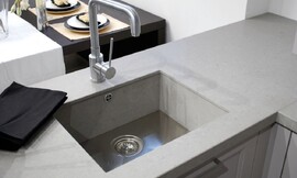 Hier ziet u een gootsteen die van hetzelfde materiaal gemaakt is als het aanrechtblad, en niet boven de rand van het werkblad uitkomt. De gootsteenstop is tegelijk een filter voor grove voedselresten. Zo wordt verstopping voorkomen. Zuordnung: Stil Design-keukens, Planungsart Keuken met zitgelegenheid