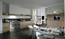 Landelijke keuken met modern accent. Hier ziet u wat een groot fornuis, typisch voor landelijke keukens, voor de keuken betekent. Hier is de afzuigkap onopvallend verwerkt in een schouw. De kasten hebben relatief brede wangen en een stenen aanrechtblad. Zuordnung: Stil Landelijke keukens, Planungsart Keuken met keukeneiland