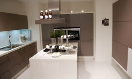 U-vormige keuken met kookeiland in het midden. Mat grijze fronten en witte aanrechtbladen. De inductie-kookplaten bevinden zich op het kookeiland voor een praktische workflow. Zuordnung: Stil Design-keukens, Planungsart Keuken met zitgelegenheid
