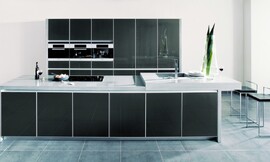 Elegantie en rechtlijnigheid in een donkere metallic tint achter glas met net aluminium kader. Hier ziet u ook het bijzondere effect van een aanrechtblad met verschillende hoogten. Rechts ziet u het verhoogde deel met de spoelbak en de eetbar. Zuordnung: Stil Klassieke keukens, Planungsart U-vormige keuken