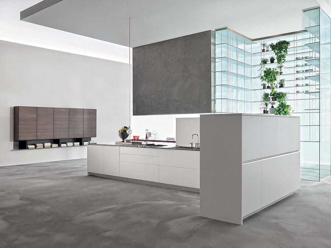 Strakke lijnen zonder onnodige versierselen, helder wit en een moderne uitstraling zijn de kenmerken van deze keuken in eilandvorm. Het rechte keukenblok bestaat uit onderkasten met deurtjes en grote lades die ideaal zijn voor het opbergen van serviesgoed, potten en pannen. De rechterhoek van de keuken wordt omsloten door half hoge kasten. Op de achtergrond is een zeer bijzonder glazen open kastsysteem te zien dat aan het plafond is opgehangen. Zuordnung: Stil Design-keukens, Planungsart Detail keukenontwerp