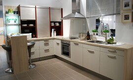 Deze gezellige L-vormige keuken biedt zeven onderkasten met beige structuurlak. Op het stompe gedeelte van de L-vorm zijn drie opzetkasten geplaatst die voorzien zijn van praktische rolluiken. Aan dit gedeelte sluit een bar in houtoptiek aan, zodat hier een zitgelegenheid voor twee personen wordt geboden. Het fornuis, de oven en de spoelbak zijn opgnomen in het langere gedeelte van de L-vorm. Zuordnung: Stil Klassieke keukens, Planungsart Keuken met keukeneiland
