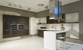 Deze moderne keuken leunt optisch op het contrast tussen sepia bruine kasten en een wit aanrechtblad, bar en achterwand. De apparatuurkast links is zwevend gemonteerd tegen een grijze strook. Zuordnung: Stil Moderne keukens, Planungsart Keuken met zitgelegenheid