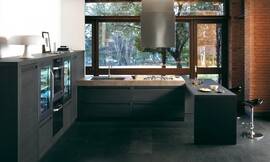 Overzichtelijke keuken in U-vorm met contrast tussen mat-donkere meubels en robuust aanrechtblad. Design fronten met greeplijst. Met simpele bar en zitgelegenheid voor interactie tijdens het koken. Design afzuigkap in het plafond. Zuordnung: Stil Moderne keukens, Planungsart keukenblok