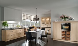 Hier ziet u een landelijke keuken in een L-opstelling met een extra blok met half hoge kasten. De kaderfronten met lichte houttint en de vakken met manden versterken het landlijke effect van deze keuken. De vier grote en twee normale lades onder het fornuis bieden genoeg plaats voor het kookgerei. In hetzelfde deel van de keuken bevindt zich ook de spoelbak. In het andere deel van de L-opstelling zijn er opzetkasten geplaatst, die de landelijke keuken ook een klassieke touch geven. De oven en koelapparatuur zijn opgenomen in de halfhoge kasten. Zuordnung: Stil Landelijke keukens, Planungsart Keuken met keukeneiland