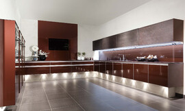 De keuken als zwevend element in de ruimte. Spanningsvolle architectuur in vorm en kleur. Achter glas de trendkleur robijn metallic. En als uniek kenmerk het variabele kastsysteem "Volare" met schuifdeuren van echte leisteen. Zuordnung: Stil Design-keukens, Planungsart Keuken met zitgelegenheid