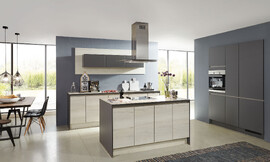 De overgang naar het woondeel bij deze keuken is vloeiend. Deze tijdloze woonkeuken is met greeploze fronten in vriendelijk houtoptiek en een keukeneiland uitgerust. Zuordnung: Stil Klassieke keukens, Planungsart L-vormige keuken