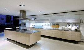 Design keuken met erg dunne greeploze fronten en aanrechtbladen. Het kookeiland staat op poten en heeft een kookveld, hier met stoomkoker uitgevoerd. Verlichting met spots in het plafond. Zuordnung: Stil Design-keukens, Planungsart U-vormige keuken
