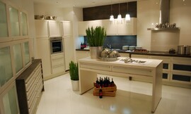 Deze keuken laat u zien wat u met een relatief grote ruimte kunt doen. Verschillende keukenmeubels tegen de wanden en een keukeneiland in het midden. Crèmetinten domineren deze keuken. Het aanrechtblad heeft een donkerdere tint. De fronten hebben brede grepen voor een iets traditionelere look. De kast links heeft glazen deurtjes. Zuordnung: Stil Moderne keukens, Planungsart L-vormige keuken