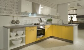 L-vormige keuken met mango gele en witte fronten en een grijs granieten aanrechtblad. De afzuigkap past onopvallend tussen de andere bovenkasten en de spoelbak op het uitstekende keukenblok is voorzien van een glasplaat om spetters tegen te houden. Zuordnung: Stil Moderne keukens, Planungsart Keuken met zitgelegenheid