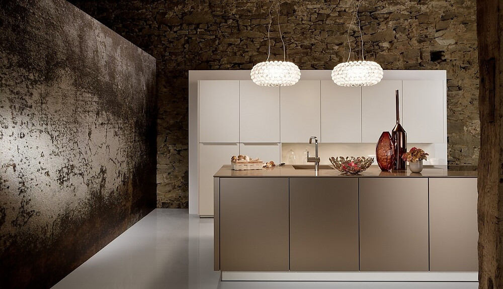Deze luxe keuken, bestaande uit een hoge keukenwand en een keukeneiland, werkt kalm door de beige en crème-tint. Het ontwerp is symmetrisch en de meubels zijn onverstoord door grepen of versieringen. Zuordnung: Stil Luxe keukens, Planungsart Keuken met keukeneiland