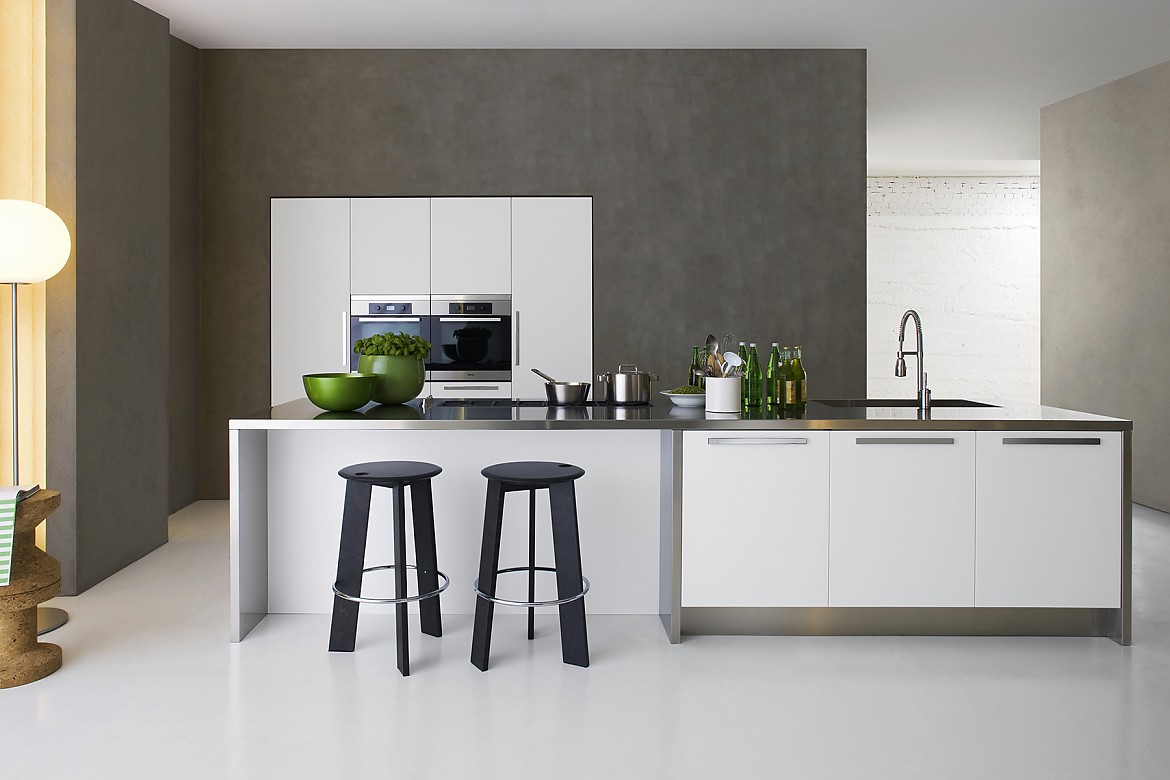 Deze zwevende keuken werkt dankzij een roestvrij stalen aanrechtblad bijzonder modern. Witte fronten met nette grepen. Het contrast van de strakke witte en metallic tinten met het donker grijze stucwerk valt op. Het aanrecht heeft een subtiele handdouche. Zuordnung: Stil Design-keukens, Planungsart Keuken met keukeneiland