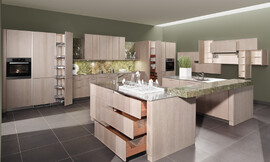 Moderne behaaglijkheid en absolute elegantie. Het oppervlakte is gebeitst in de tint "zilver eik", waardoor deze topkeuken herinnert aan de natuurlijkheid van oude versleten houtplanken. Het binnenwerk van de lades in massief notenhout biedt een aangenaam, warm contrast met de koelere tint van de buitenkant van de meubels. Zuordnung: Stil Moderne keukens, Planungsart keukenblok