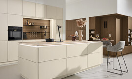 Deze keuken combineert een tijdloos-modern ontwerp met een greeploze afwerking en een mat, licht unidecor. Door een functioneel ontwerp met eiland en bar biedt deze keuken een perfecte balans tussen esthetiek en gebruiksgemak. Zuordnung: Stil Moderne keukens, Planungsart Keuken met keukeneiland