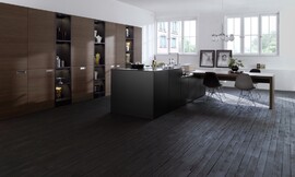 Vrijwel niet meer te herkennen als keuken, doordat o.a. de apparatuur achter hoge houten schuifdeuren in de wand is aangebracht. Het kookeiland is strak vormgegeven, zwart van kleur en zonder enige tierelantijnen. Het fornuis en de spoelbak met mengkraan vallen nauwelijks op. Aan één kant is het kookeiland iets lager gemaakt. Daarop ligt het hout voor een lange eettafel. Al met al een terughoudende keuken die prima in een woonruimte past. Zuordnung: Stil Moderne keukens, Planungsart L-vormige keuken