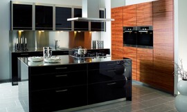 Deze keuken bestaat uit twee keukenblokken die tegen de wand geplaatst zijn en een apart kookeiland. In een van de twee keukenblokken met het natuurlijke tineo fineer, met duidelijke houtstructuur, is de apparatuur op praktische werkhoogte opgenomen. Het kookeiland en het andere keukenblok zijn voorzien van een in 13 stappen vervaardigde zwarte hoogglans lak, waardoor een spannend contrast met de houtoptiek van de hoge apparatuurkasten is ontstaan. Het roestvrij staal van de sokkels komt weer terug in de vijf hangkasten boven de spoelbak, die samen met de onderkasten en de grote lades voor voldoende bergruimte zorgen. Zuordnung: Stil Landelijke keukens, Planungsart Open keuken (woonkeuken)