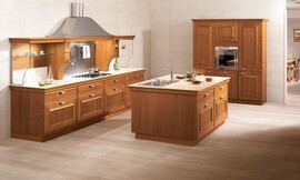 Landelijke keuken met warme houttinten en cassettefronten. Een keukeneiland met wasbak maakt deze keuken open en communicatief. De belangrijkste keukenwand heeft een brede afzuigkap in een riante schouw en planken van glas voor servies. Zuordnung: Stil Landelijke keukens, Planungsart L-vormige keuken