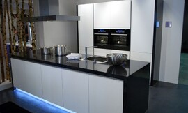 Design keuken met hoogglans zwarte wangen en aanrechtblad. Greeploze fronten en opvallende blauwe verlichting uit de sokkel van het keukeneiland. Zuordnung: Stil Design-keukens, Planungsart Detail keukenontwerp