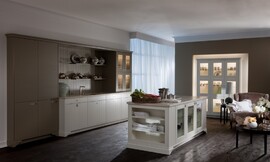 Deze landelijke keuken met keukeneiland is subtiel afgewerkt: opvallende sokkels, een dun aanrechtblad, een bijzondere structuur van de poriën van het houtfineer, etc. De fronten hebben onopvallende grepen en zijn hier in gebroken wit en lichtbruin uitgevoerd. Zuordnung: Stil Landelijke keukens, Planungsart Open keuken (woonkeuken)