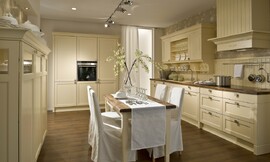 In deze keuken ziet u enkele typische ornamenten toegepast in landelijke keukens. Behalve cassette fronten ziet u bijvoorbeeld een schouw, opvallende sokkels en afgeronde lijsten aan de bovenkanten van de meubels. Hier uitgevoerd met een passende eetkamertafel. Zuordnung: Stil Landelijke keukens, Planungsart U-vormige keuken
