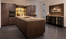 Een perfecte mix van tijdloze moderniteit en hoge functionaliteit. Deze greeploze keuken biedt een L-vormig ontwerp en een elegant donker hout frontdecor met stenen aanrecht. Zuordnung: Stil Design-keukens, Planungsart Keuken met keukeneiland