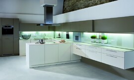 Deze keuken in F-vorm (!) valt op door het contrast tussen gebroken witte onderkasten, brons-bruine bovenkasten en een verlichte glazen keukenachterwand. Een gedeelte van de keukenwand zweeft boven de grond. Boven het centrale kookgedeelte hangt een opvallende afzuigkap. De keuken heeft een dun aanrechtblad dat optisch niet opvalt. Zuordnung: Stil Moderne keukens, Planungsart U-vormige keuken