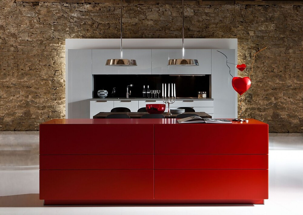 Een simpel, symmetrisch maar elegant keukenblok tegen de wand wordt afgemaakt met een afgestemde tafel en rood kastmeubel. De buitenste rij kasten is greeploos en de lades in het midden hebben horizontale grepen. Simpele witte fronten contrasteren met de felrode kast in de voorgrond. Zuordnung: Stil Luxe keukens, Planungsart Keuken met keukeneiland