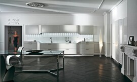 L-keuken met groot, symmetrisch keukenblok. Witte fronten met horizontale grepen. Werkblad met hoogteverschillen en verlichting vanuit de bovenkast. Verschillende rondingen in het kastontwerp. Zuordnung: Stil Design-keukens, Planungsart L-vormige keuken