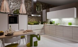 Deze lichtvoetige keuken in de L-vorm speelt met een subtiel contrast tussen lichte houttinten en gebroken witte vlakken. Fronten met greeplijsten houden de keuken optisch kalm. Er ontstaat een bijzonder contrast tussen de kalme design keuken en de ruwe stenen muur. Links zijn half hoge kasten geplaatst met daarin de apparatuur. Daarnaast is het fornuis met daaronder handige grote lades voor alle potten, pannen en ander kookgerei. Na de hoek komt er een blok met onderkasten, de spoelbak en daarboven de kasten met zeer brede deurtjes. Onder de hangkasten zijn handige spots aangebracht, zodat er altijd genoeg licht op het aanrechtblad schijnt. Zuordnung: Stil Klassieke keukens, Planungsart Keuken met keukeneiland
