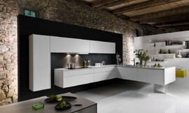 In deze moderne zwevende designkeuken komt de L-vorm twee keer terug. Eén keer als hoge kast tegen de muur met twee brede bovenkasten daarnaast. Ook het ondergedeelte vormt een L. Op het ene gedeelte van de L kan er worden gekookt, de afzuigkap is in de kast daarboven vrijwel onzichtbaar opgenomen. Het andere deel van de L is o.a. voorzien van de spoelbak. De greeploze strakke kasten en het dunne aanrechtblad zorgen voor een rustige uitstraling. Zuordnung: Stil Luxe keukens, Planungsart Open keuken (woonkeuken)