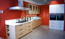 Moderne keuken met eiken houten cassette fronten. Het fornuisgedeelte komt circa 20 cm naar voren ten opzichte van de rest van het aanrecht. Het witte aanrechtblad is verbonden met een eveneens wit achterwandje van 15 cm. Bovenkasten met glazen deurtjes. Zuordnung: Stil Moderne keukens, Planungsart Detail keukenontwerp