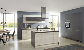 De overgang naar het woondeel bij deze keuken is vloeiend. Deze tijdloze woonkeuken is met greeploze fronten in vriendelijk houtoptiek en een keukeneiland uitgerust. Zuordnung: Stil Moderne keukens, Planungsart keukenblok