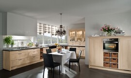 Hier ziet u een landelijke keuken in een L-opstelling met een extra blok met half hoge kasten. De kaderfronten met lichte houttint en de vakken met manden versterken het landlijke effect van deze keuken. De vier grote en twee normale lades onder het fornuis bieden genoeg plaats voor het kookgerei. In hetzelfde deel van de keuken bevindt zich ook de spoelbak. In het andere deel van de L-opstelling zijn er opzetkasten geplaatst, die de landelijke keuken ook een klassieke touch geven. De oven en koelapparatuur zijn opgenomen in de halfhoge kasten. Zuordnung: Stil Landelijke keukens, Planungsart L-vormige keuken