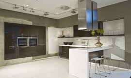 Deze moderne keuken leunt optisch op het contrast tussen sepia bruine kasten en een wit aanrechtblad, bar en achterwand. De apparatuurkast links is zwevend gemonteerd tegen een grijze strook. Zuordnung: Stil Landelijke keukens, Planungsart U-vormige keuken
